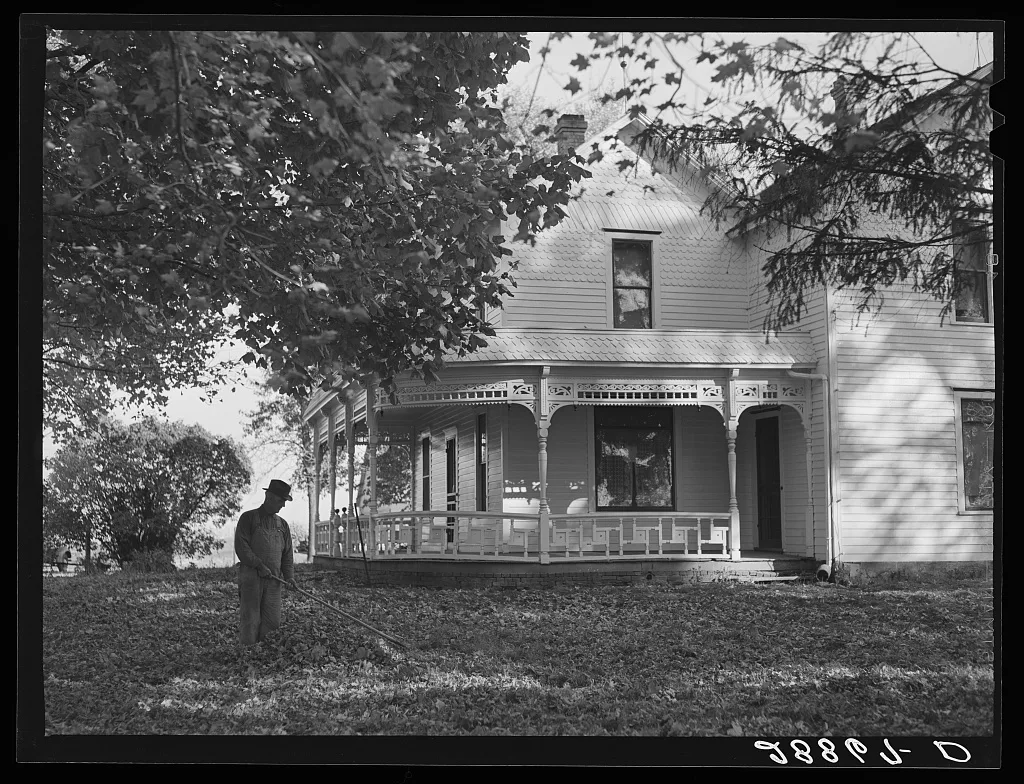 Farmer raking leaves on lawn of his home. Grundy County, Iowa, 1939