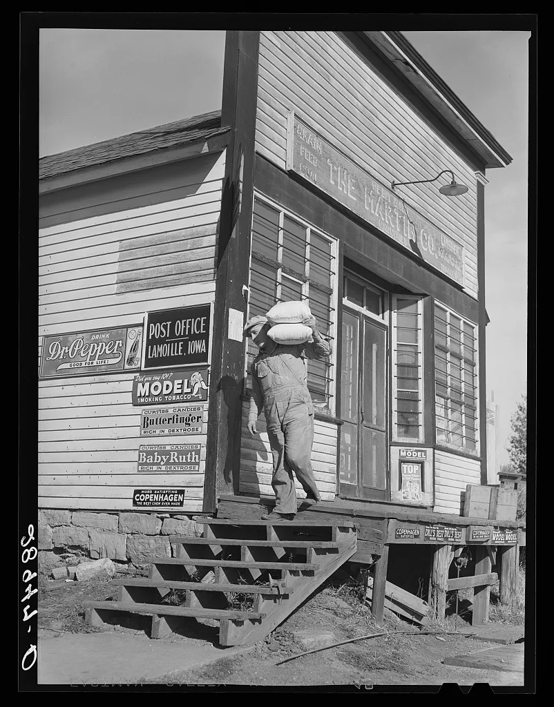 Carrying bags of flour out of general store. Lamoille, Iowa, 1939