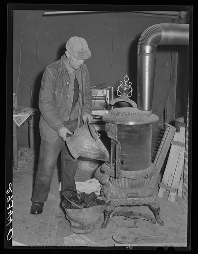 O.G. Haubeil emptying coal scuttle into stove. Ross County, Ohio, 1940